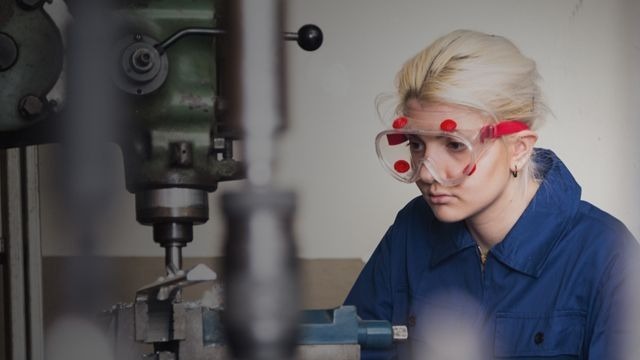 Young woman working on machine wearing personal protective equipment