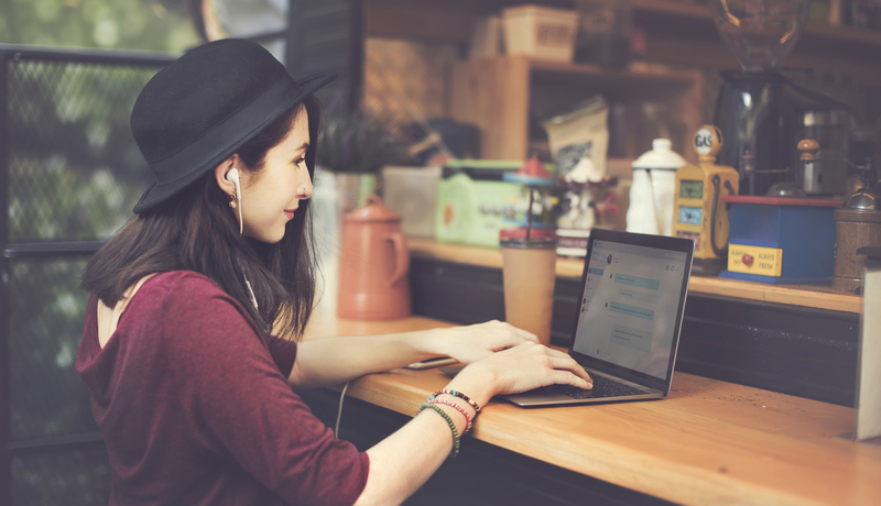 Young woman in hat working on a laptop in outdoor coffee shop